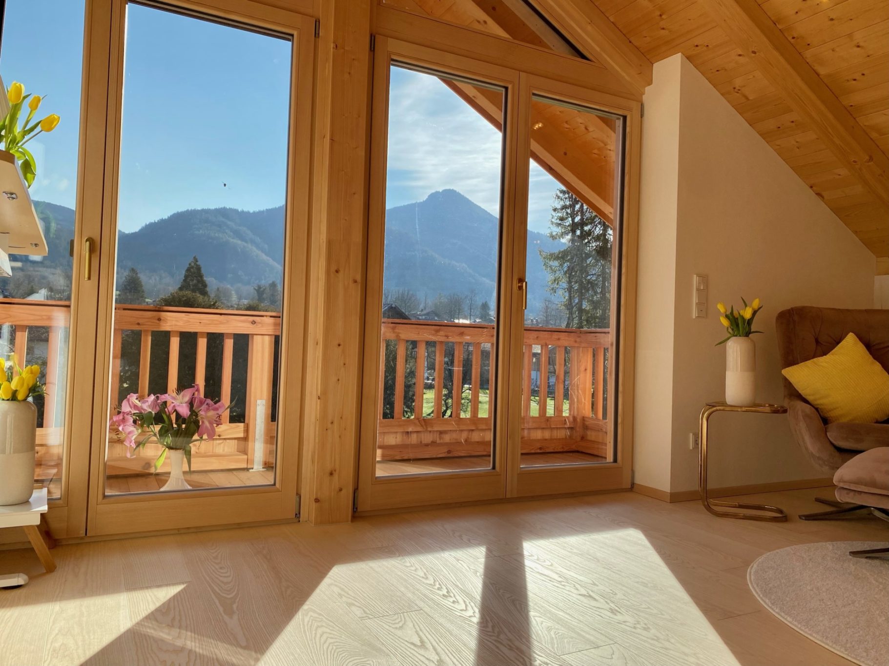 Coaching in Lenggries Heller Wohnraum mit großen Fenstern, Blick auf Berge und bunten Blumen im Vordergrund.